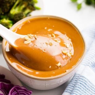 white spoon being dipped into vegan peanut sauce, broccoli in background.