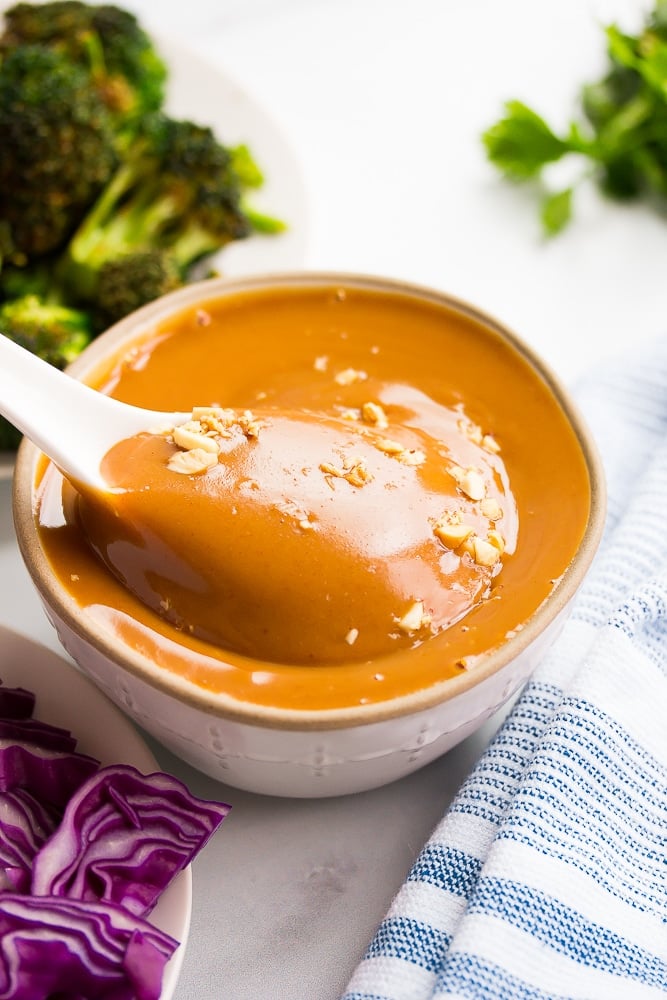 white spoon being dipped into vegan peanut sauce, broccoli in background.