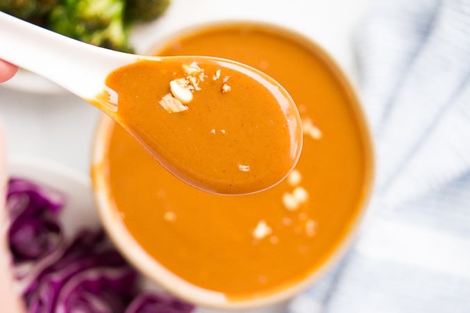 bowl with peanut sauce and white spoon close up full of the sauce.
