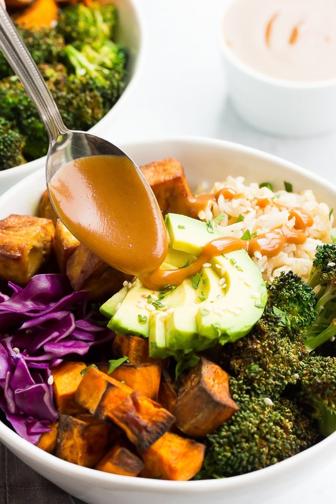 buddha bowl with rice, vegetables and tofu with vegan peanut sauce drizzling on top with a spoon.