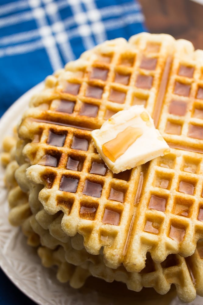 side shot of stack of waffles with syrup and butter