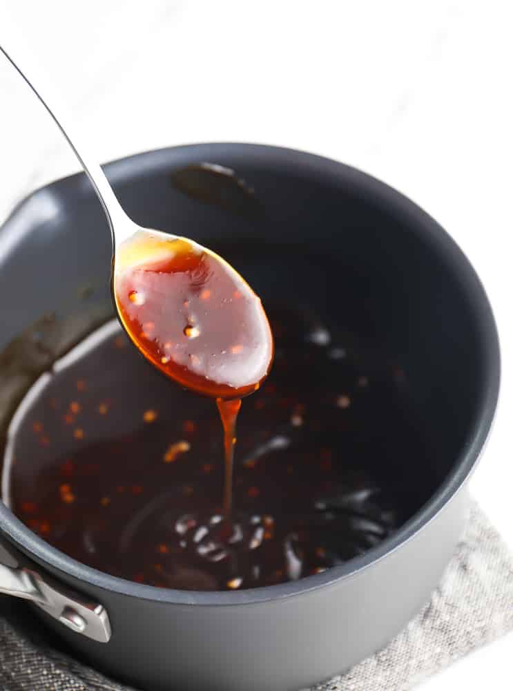 a metal spoon taking a scoop of teriyaki sauce from a black pot.