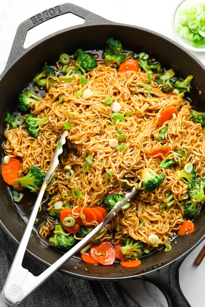 teriyaki noodles with vegetables and metal tongs in a large black skillet.