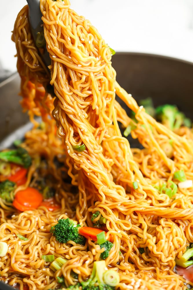 tongs picking up teriyaki noodles from a large skillet.