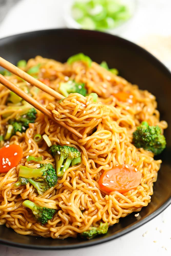 chopsticks picking up a bite of teriyaki noodles from a bowl.