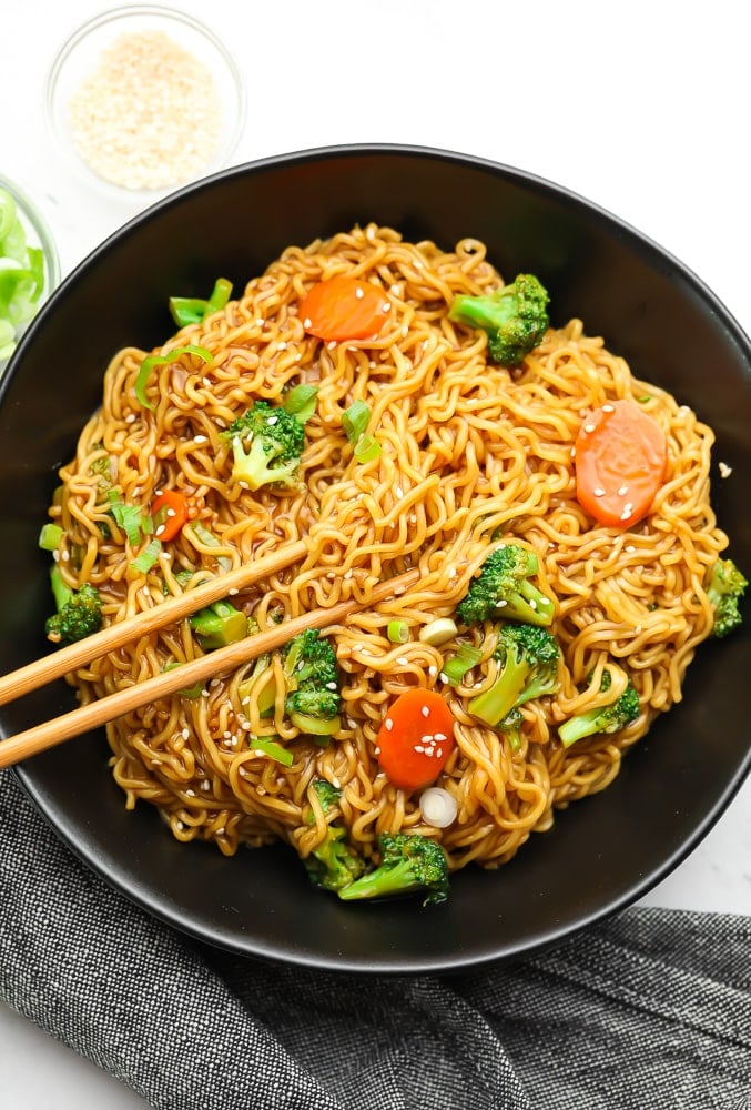 overhead view of teriyaki noodles with vegetables and chopsticks in a black bowl.