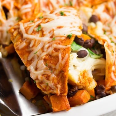 close up of enchilada casserole in white dish, piece being removed