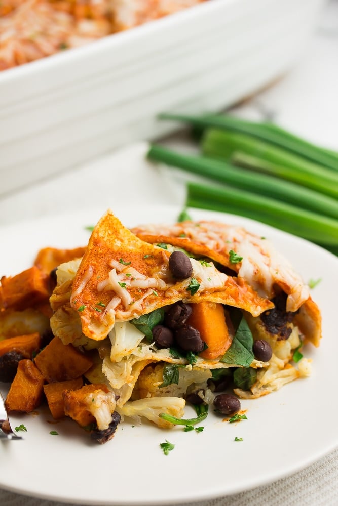 piece of vegan enchilada casserole on a white plate, green onions in background