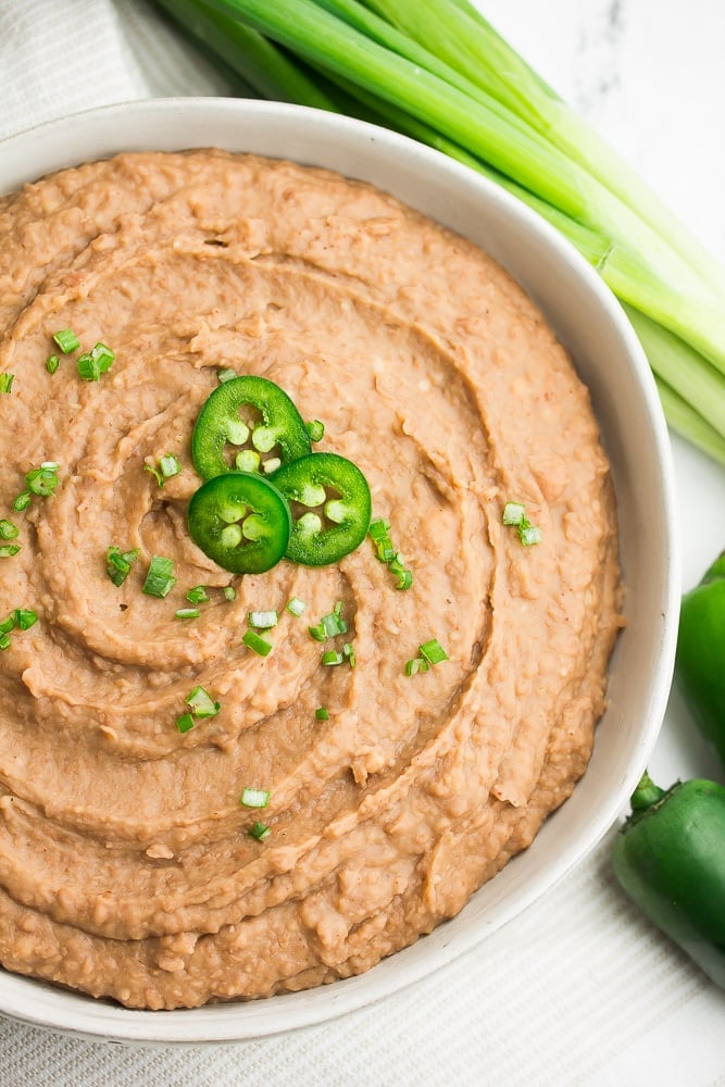 a white bowl full of refried beans with jalapenos sliced on top and green onions.