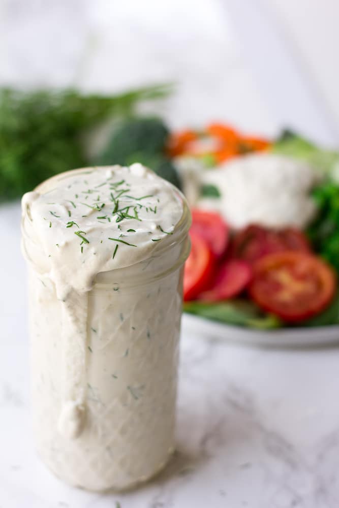 vegan ranch in a glass jar with salad behind it