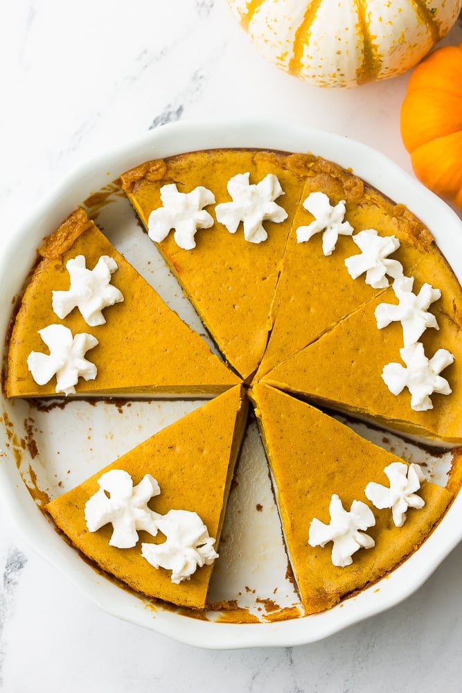 lookin down on a pumpkin cheesecake with whipped cream, cut into slices in pan.