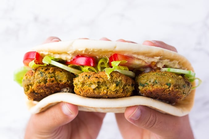 vegan falafel in flatbread with veggies and hands holding it