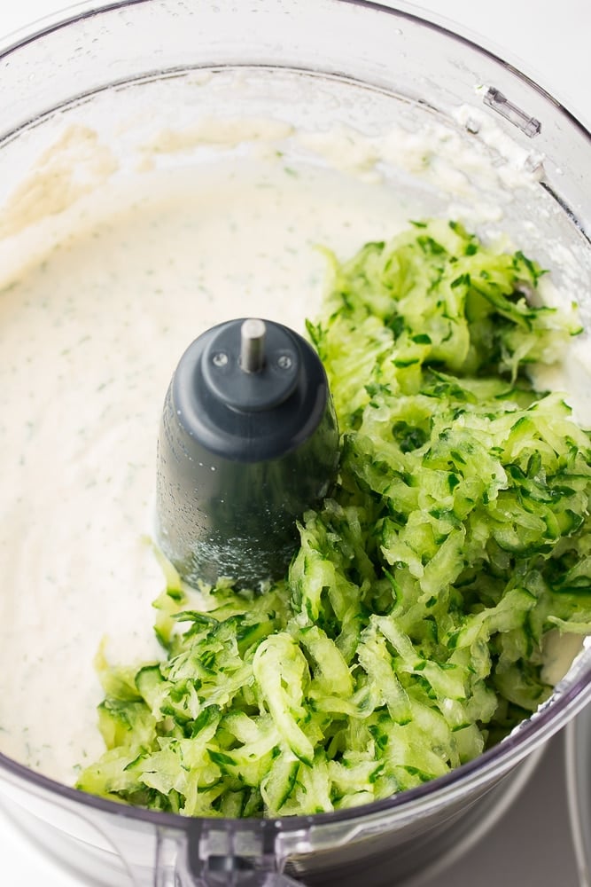 food processor with creamy sauce and grated cucumber not yet blended in