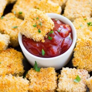 tofu nuggets being dipped into ketchup, no hand, with more nuggets all around.