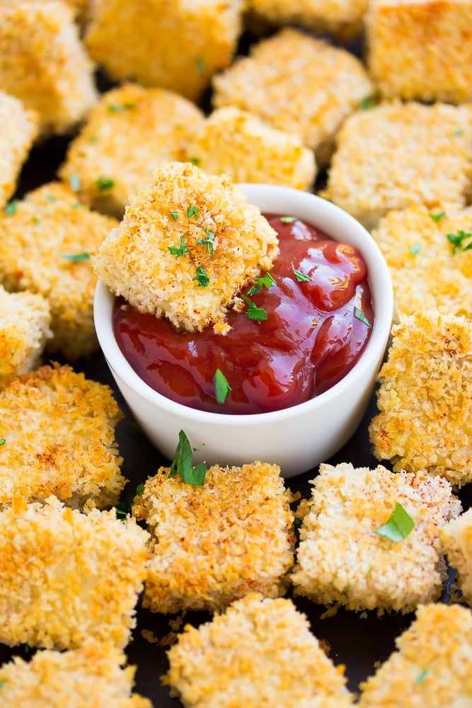 tofu nuggets being dipped into ketchup, no hand, with more nuggets all around.