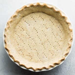 square image of cooked pie crust, fluted edges, fork holes in the middle on a grey background