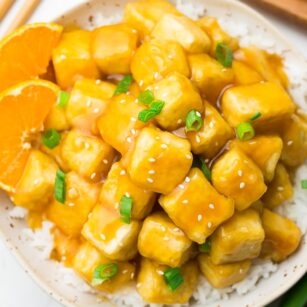 orange tofu on top of rice on a white plate