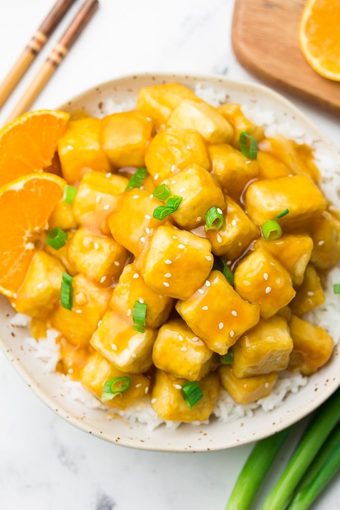 orange tofu on top of rice on a white plate