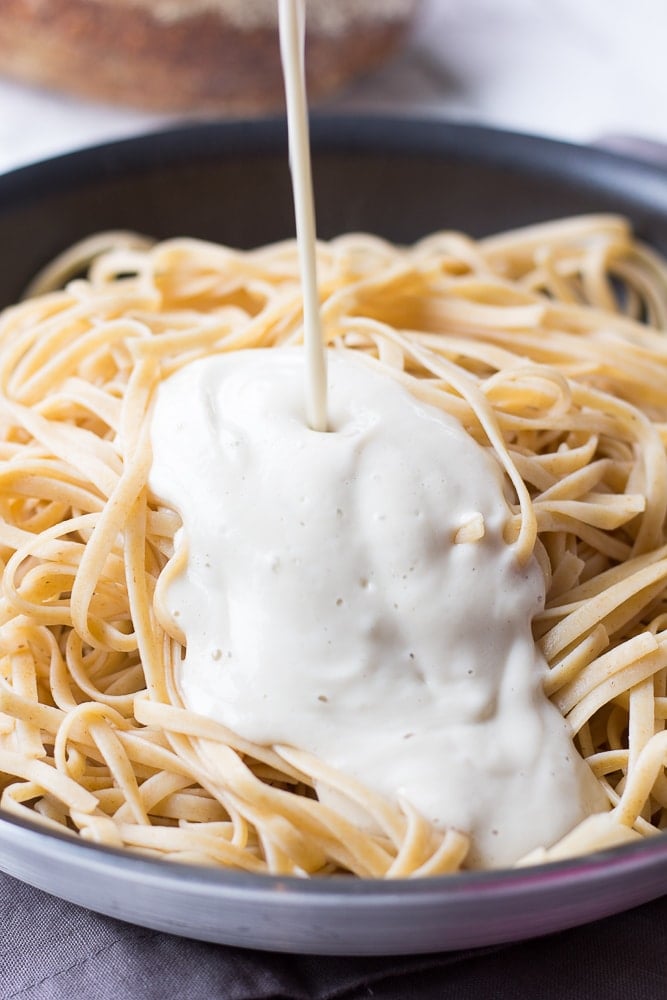 vegan alfredo sauce being poured in a pot of fettucine noodles