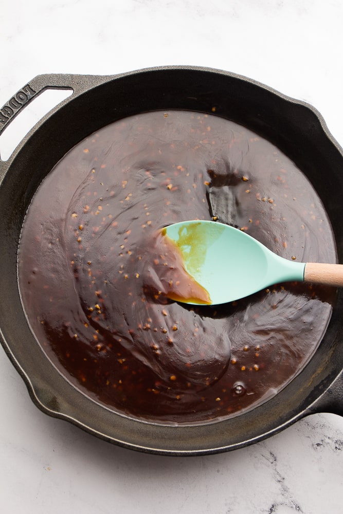 sticky sauce in a cast iron pan being stirred