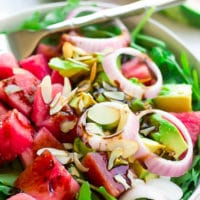 arugula watermelon salad with onions and avocado in a bowl