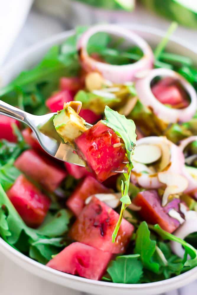 fork taking some watermelon salad with arugula from a bowl