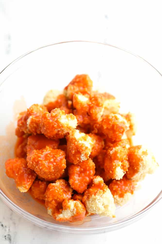 showing cauliflower that has been baked being coated in hot sauce mixture