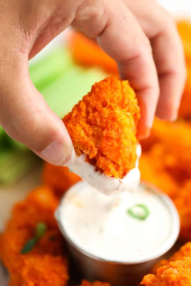a hand dipping a buffalo cauliflower into ranch dip
