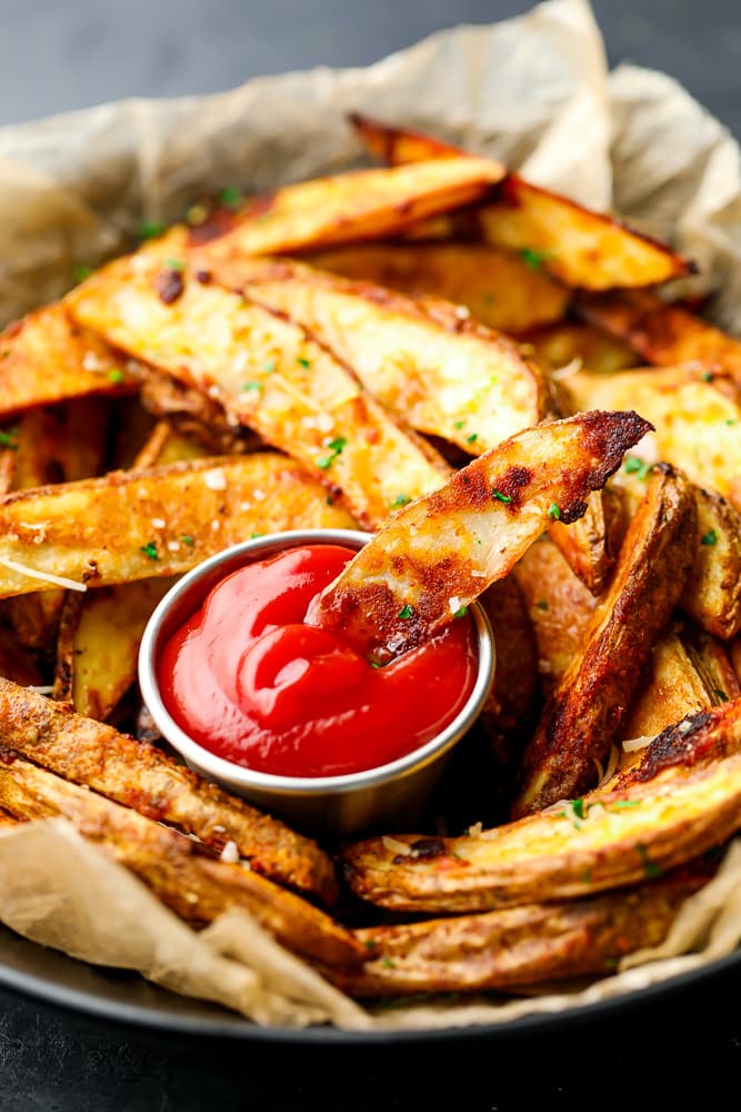 black bowl line with parchment paper and lots of wedged potatoes being dipped in ketchup