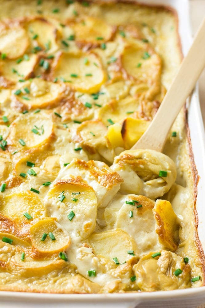 vegan scalloped potatoes in casserole dish with a wooden spoon