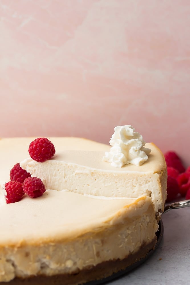 whole cheesecake with raspberries, slice being removed