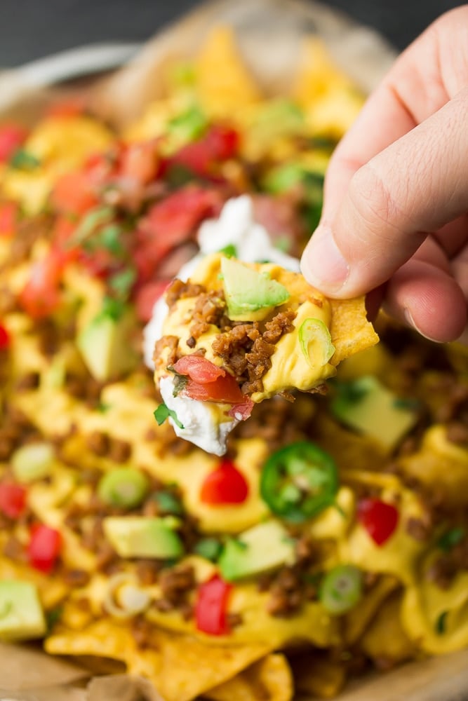 a chip loaded with toppings being pulled from a plate of nachos