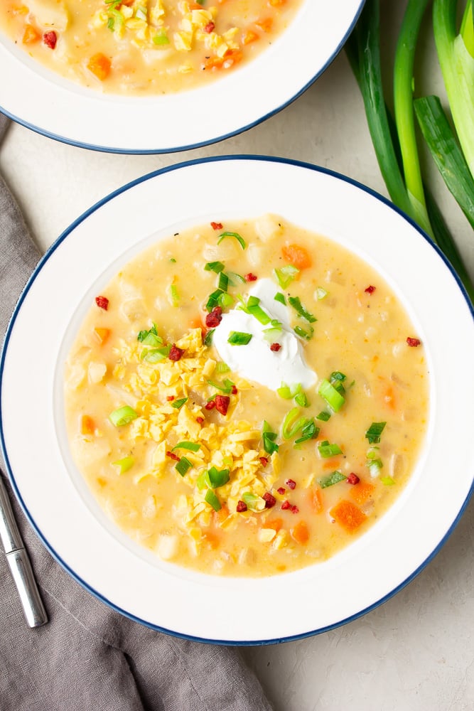 looking down on two bowls of soup, light orange in color with sour cream and cheese, chives on top