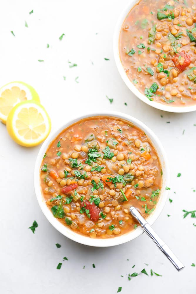 two bowls of lentil soup with lemons on white background
