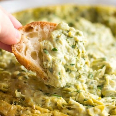 vegan spinach artichoke dip with a piece of bread dipped into it