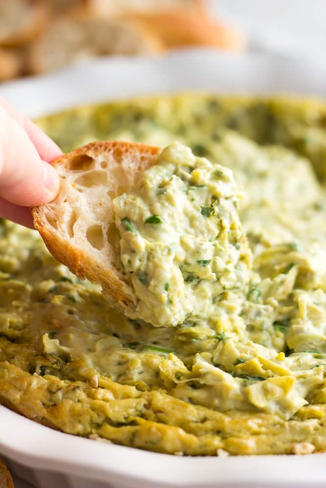 vegan spinach artichoke dip with a piece of bread dipped into it