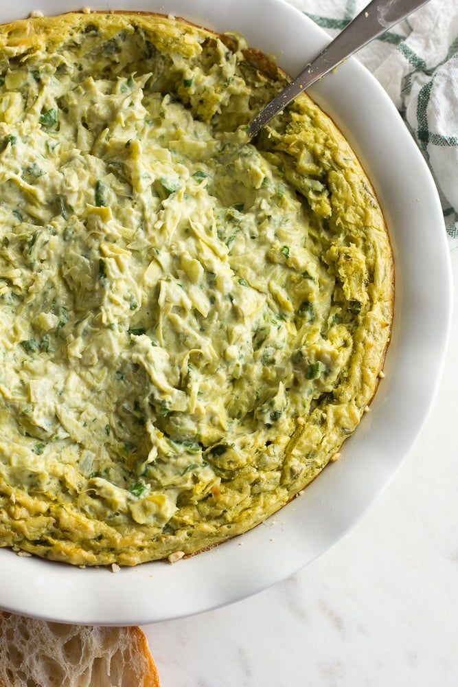 vegan spinach artichoke dip in a large bowl with a spoon