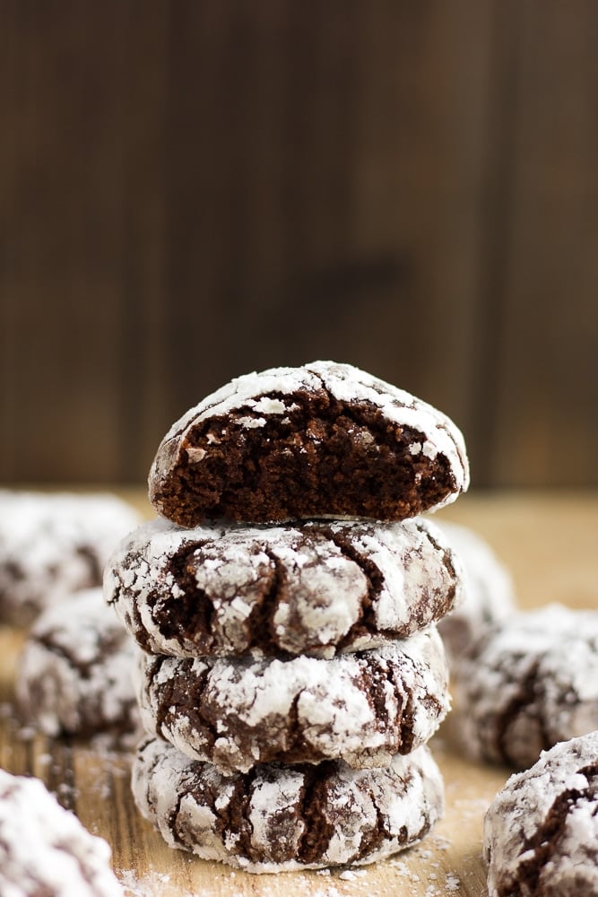 vegan chocolate crinkle cookies stacked with a bite taken out of one.