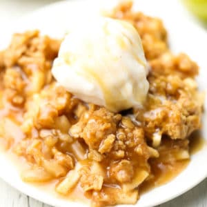 square image of apple crisp with ice cream on a plate