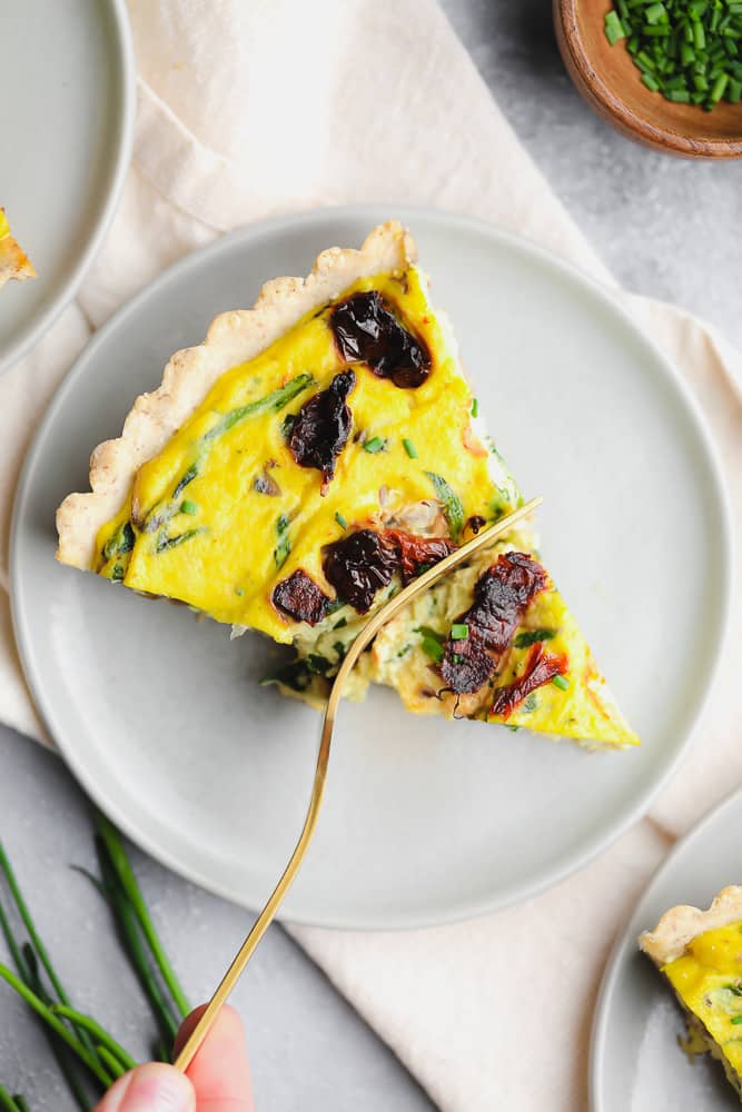 piece of quiche on a plate with a fork taking a bite