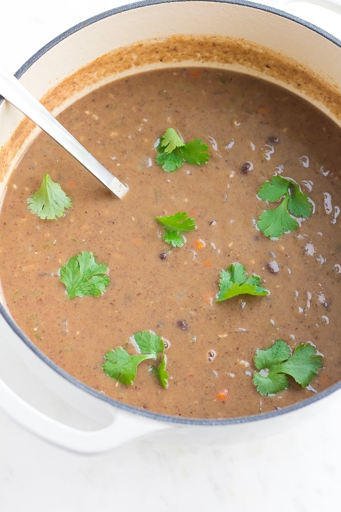 vegan black bean soup in a large white pot with cilantro in it