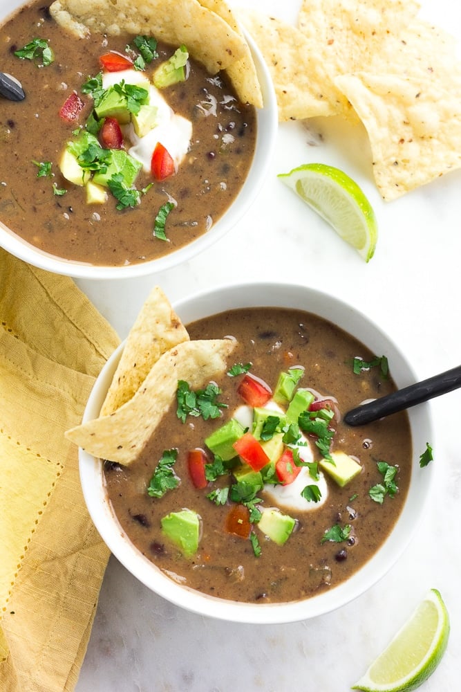 2 bowls of black bean soup with avocado, chips, tomatoes and cilantro