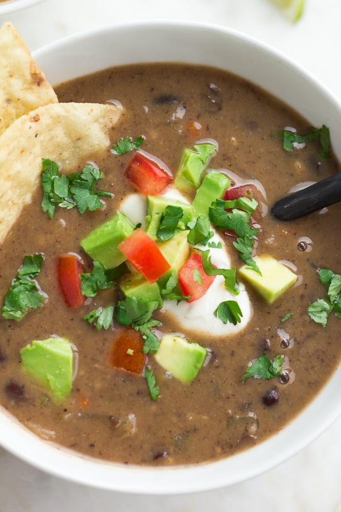 close up of bowl of black bean soup with sour cream, cilantro, chips and tomatoes