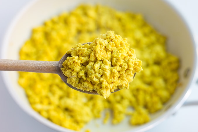 tofu scramble on a wooden spoon with pan underneath it