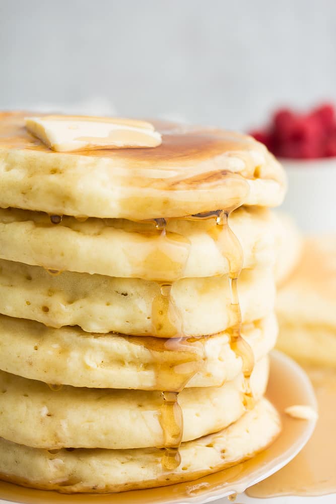 close up of side of stack of pancakes, raspberries in back