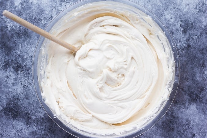 bowl of vegan cream cheese frosting with a wooden spoon.