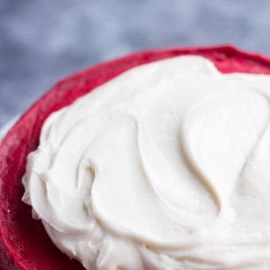 vegan cream cheese frosting being spread on a red cake.