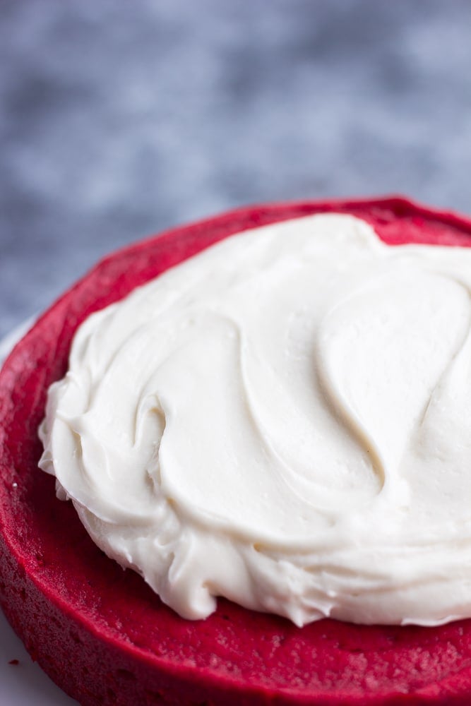 vegan cream cheese frosting being spread on a red cake.