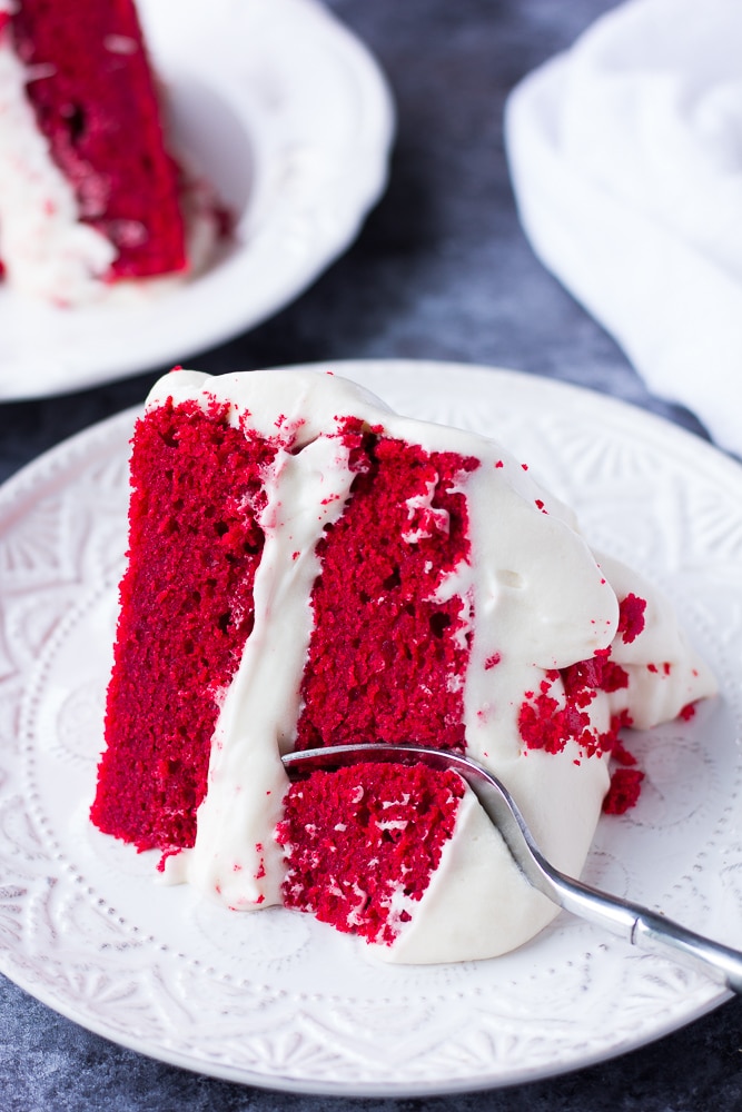slice of vegan red velvet cake on a plate with a fork in it.