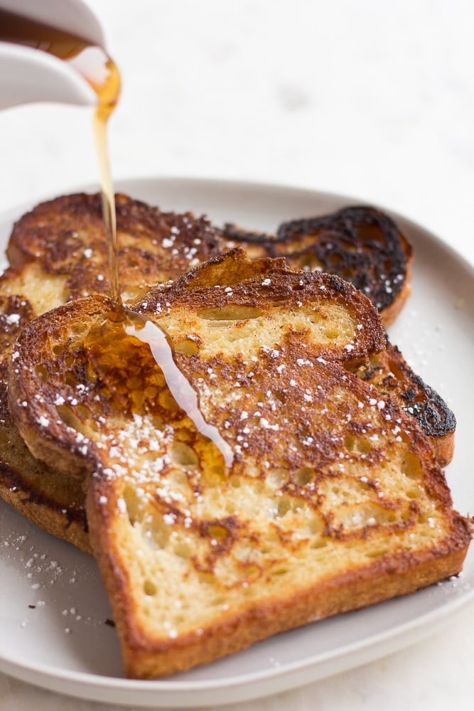 cooked vegan french toast on a plate with syrup being poured on it.